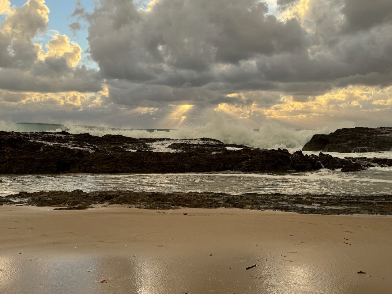 page10_img2 Stormy beach with dark rocks, crashing waves and sunbeams through heavy clouds.