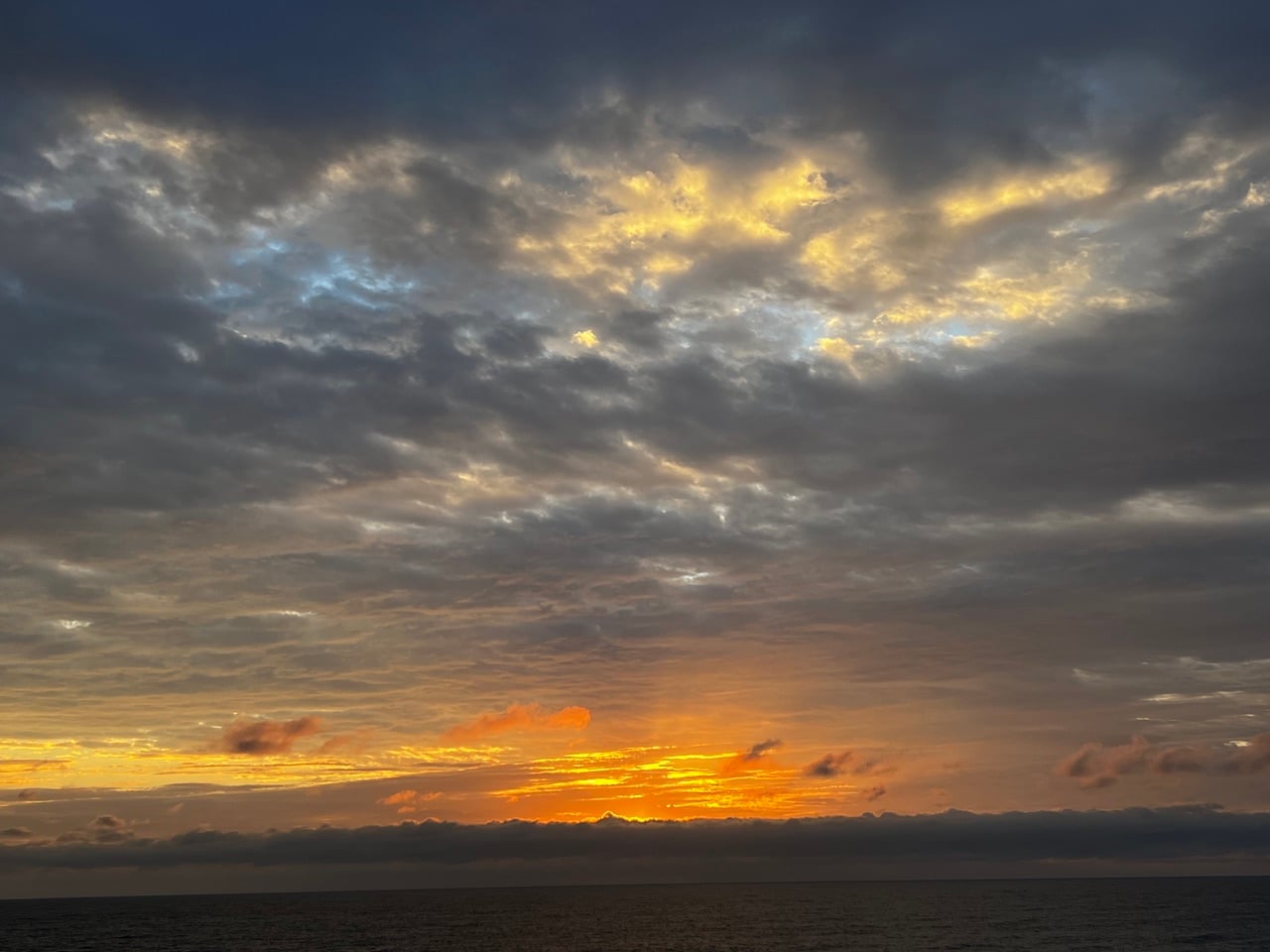 Sunset over the ocean with an orange glow along the horizon and dark clouds above.